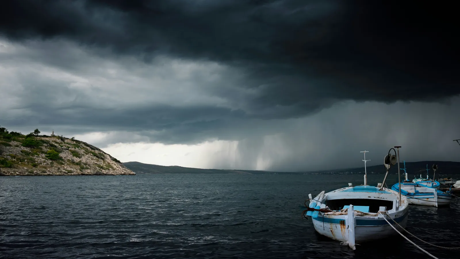 A boat at anchor as a dark rain squall sweeps across the bay behind it.