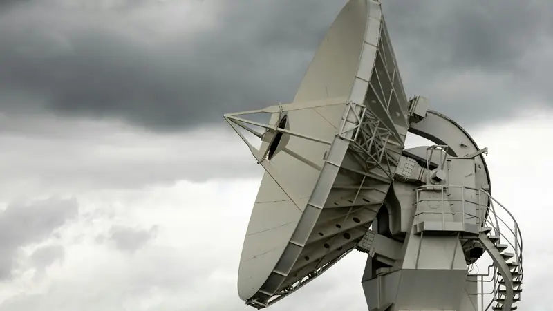 A large white satellite dish turned toward a stormy grey sky.