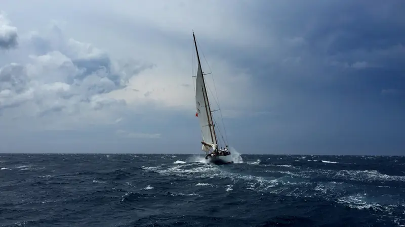 A sloop heeled over under sail in open water beneath a heavy grey sky.