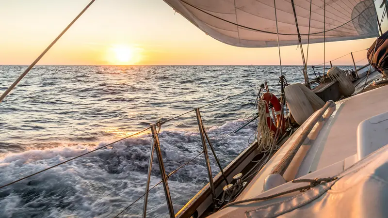 The deck of a yacht sailing toward a low sun over calm open water.